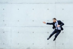 Portrait of an bearded young businessman in front of a concrete wall Businessman doing a karate kick