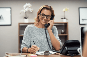 woman at desk taking notes smiling on phone
